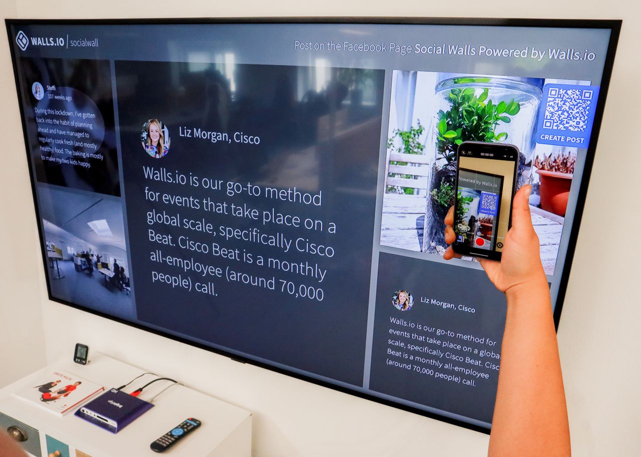 A person uses a smartphone to scan a QR code displayed on a large screen indoors.